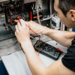An electrician uses a multimeter to test and diagnose connections in an open electrical panel.